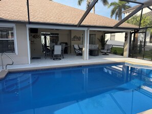 A swimming pool with a covered patio area, outdoor furniture, and a view of a residential building. - 3 bedroom home close to resturants,  beach and quick boating access. (Cape Coral)