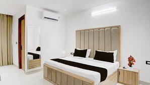 A modern bedroom with a large bed, bedside tables, a mirror, and an air conditioning unit.