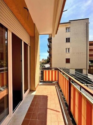 Un balcone stretto con pavimento piastrellato, ringhiera in legno e vista sui palazzi vicini.