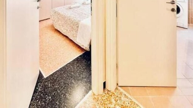 Un pasillo que lleva a un dormitorio con una cama, lavadora y una zona de cocina.