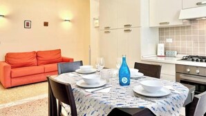 Un comedor con una mesa dispuesta para cuatro personas, una botella azul y un sofá rojo al fondo.