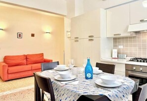 Un coin repas avec une table dressée pour quatre personnes, une bouteille bleue et un canapé rouge en arrière-plan.
