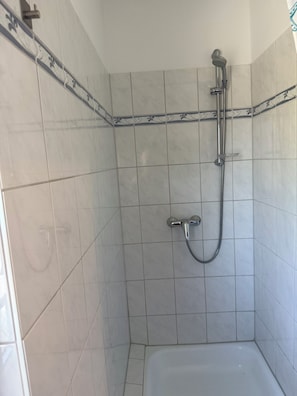 A shower with a handheld showerhead and a handheld faucet, tiled walls, and a corner shower stall.