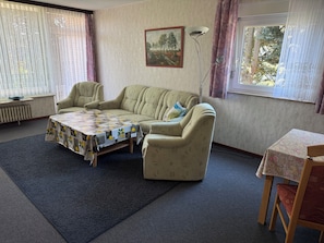 A living room with a sofa, a table with a floral tablecloth, a floor lamp, and a painting on the wall.