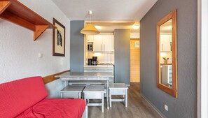 Ein kompakter Wohnraum mit einer Küchenzeile, einer Essecke mit einer Bank und einem roten Sofa.