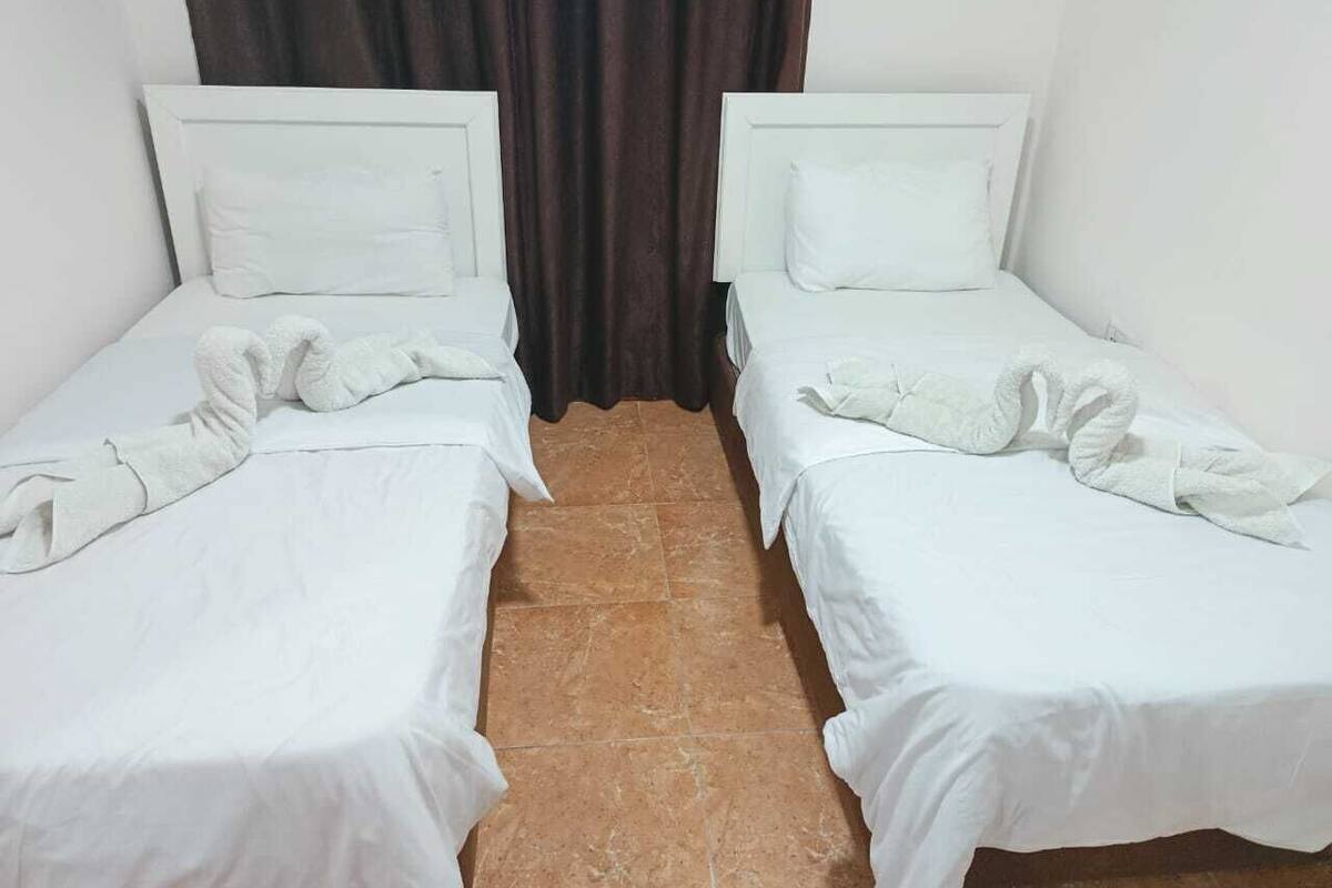 Two single beds with white linens and headboards, a brown curtain, and a tiled floor.