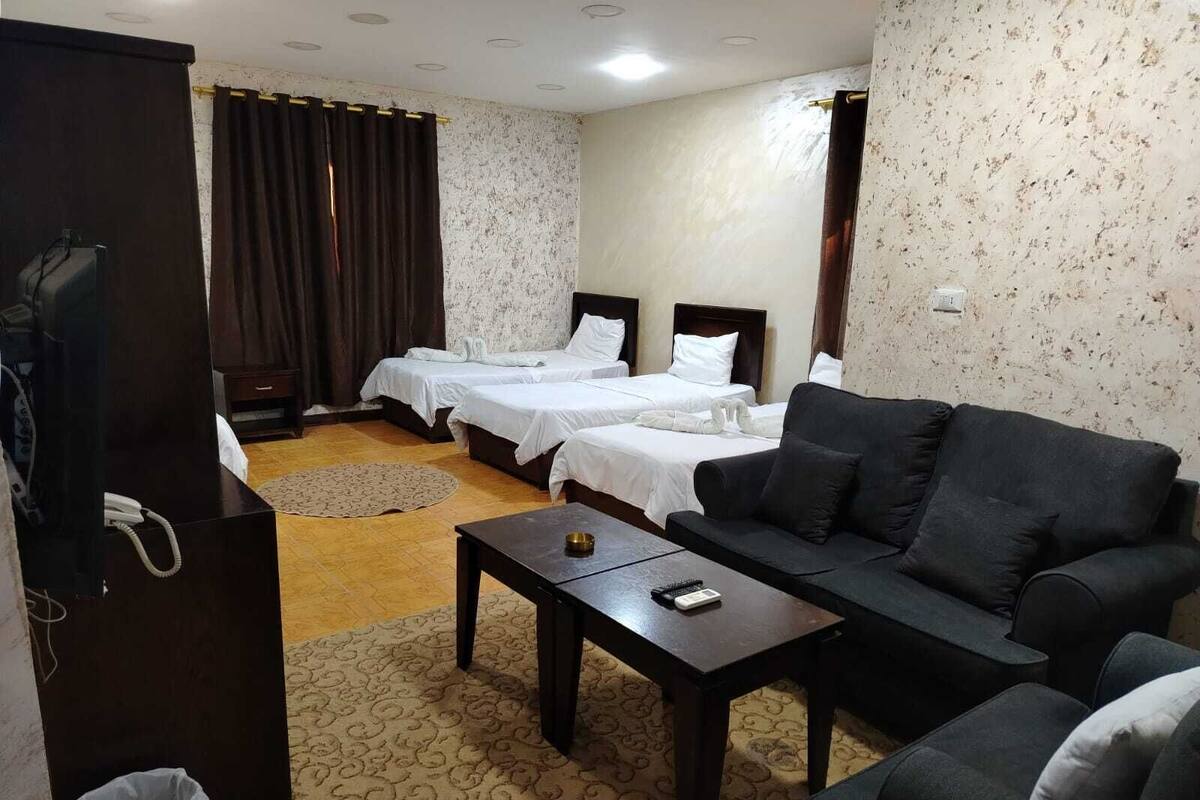 A hotel room with two beds, a sofa, a small table, a TV, and a trash bin.