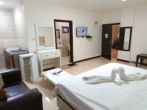 A hotel room with a bed, a desk with a chair, a small refrigerator, a mirror, a television, and a bathroom visible through an open door. - Siveen Hotel (Amman)