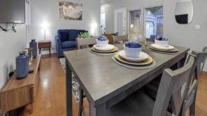Un comedor con una mesa preparada para cuatro personas, un sofá azul y un ventilador de techo.