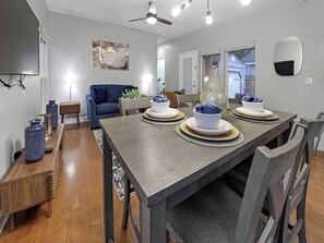 A dining area with a table set for four, a blue sofa, and a ceiling fan. - Memphis 2BR/1.5BA, Near St. Jude & Downtown, Fenced Yard, Pet-Friendly (Memphis)