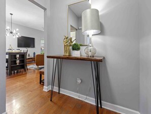 A modern living room with a wooden console table, a floor lamp, and a television mounted on the wall. - Memphis 2BR/1.5BA, Near St. Jude & Downtown, Fenced Yard, Pet-Friendly (Memphis)