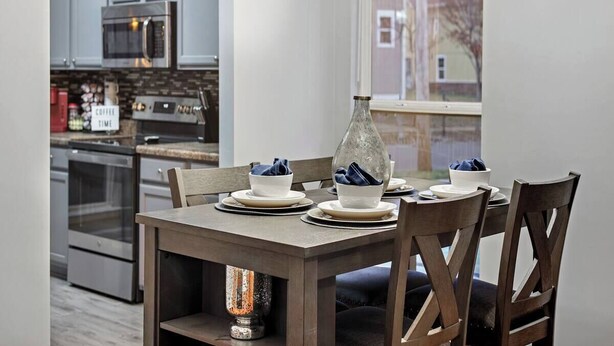 Un comedor con una mesa dispuesta para cuatro, una cocina moderna al fondo y un amplio ventanal con vistas.