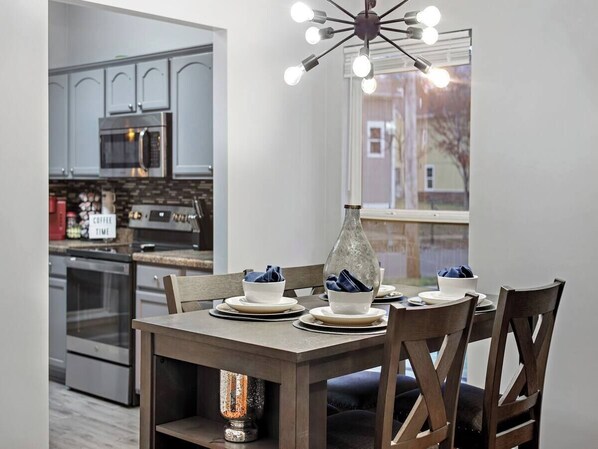 A dining area with a table set for four, a modern kitchen in the background, and a large window with a view. - Memphis 2BR/1.5BA, Near St. Jude & Downtown, Fenced Yard, Pet-Friendly (Memphis)
