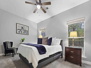 A bedroom with a bed, a chair, a nightstand, a window, and a ceiling fan. - Memphis 2BR/1.5BA, Near St. Jude & Downtown, Fenced Yard, Pet-Friendly (Memphis)