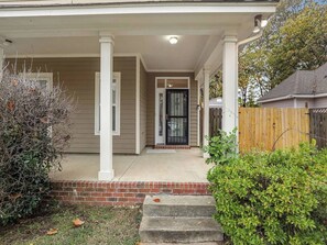 A residential house with a covered porch, a front door with a black gate, and a brick foundation. - Memphis 2BR/1.5BA, Near St. Jude & Downtown, Fenced Yard, Pet-Friendly (Memphis)
