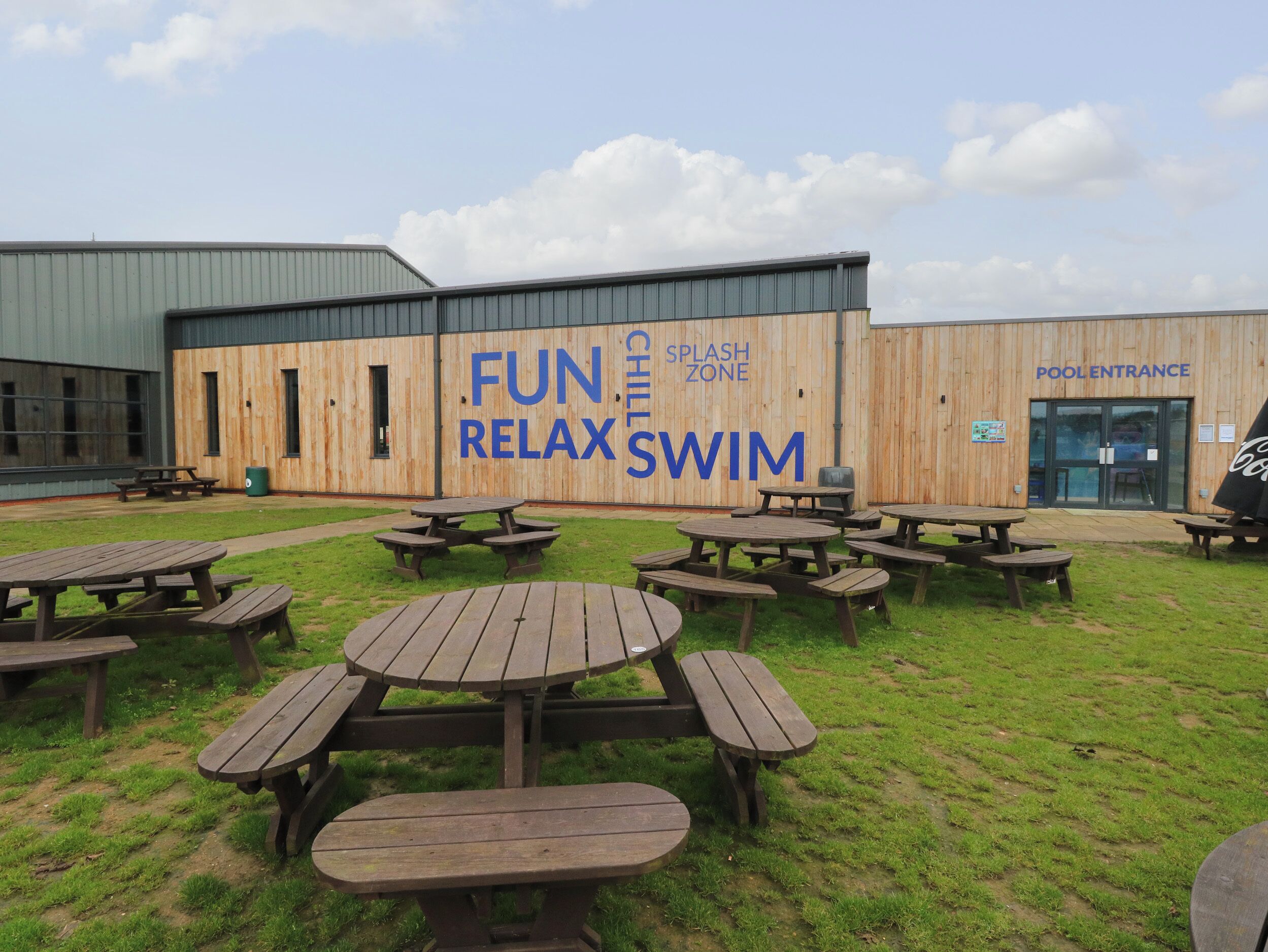 An outdoor area with picnic tables and a building with a sign that reads "FUN RELAX SWIM".