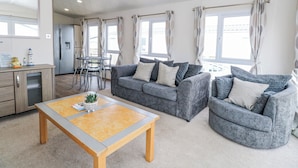 A modern living room with a grey sofa set, a wooden coffee table, and a dining area with a table and chairs. - 59 Cliff Field (Lowestoft)
