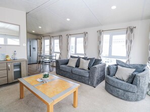 A modern living room with a grey sofa set, a wooden coffee table, and a dining area with a table and chairs. - 59 Cliff Field (Lowestoft)