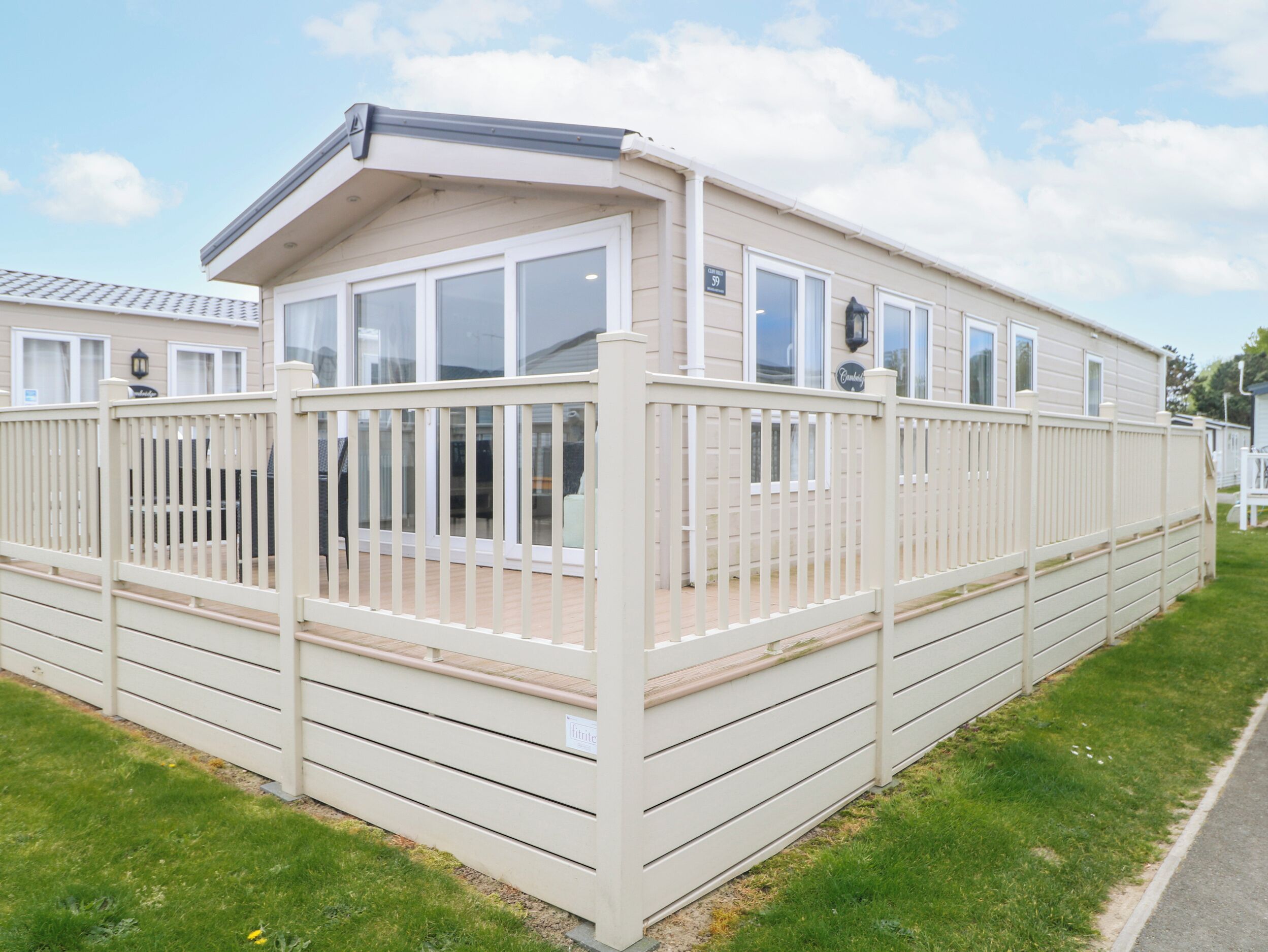 A caravan with a covered deck, a fenced patio, and a number sign indicating its unit.