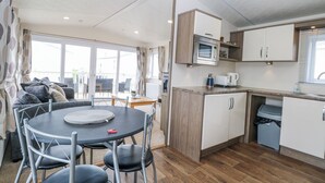 A compact kitchen with a microwave, coffee maker, and a sink. There is a dining area with a table and chairs. - 59 Cliff Field (Lowestoft)