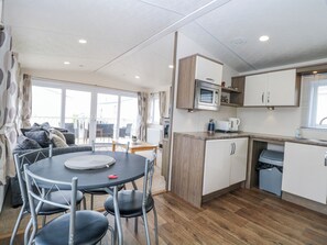 A compact kitchen with a microwave, coffee maker, and a sink. There is a dining area with a table and chairs. - 59 Cliff Field (Lowestoft)