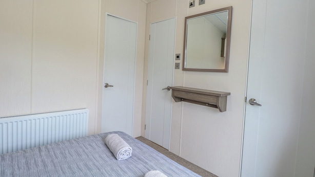 A bedroom with a bed, a mirror, a shelf, and two doors. - 59 Cliff Field (Lowestoft)