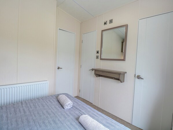 A bedroom with a bed, a mirror, a shelf, and two doors. - 59 Cliff Field (Lowestoft)