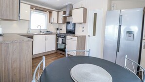 A modern kitchen with a dining table, stainless steel appliances, and wooden cabinetry. - 59 Cliff Field (Lowestoft)
