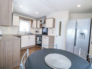 A modern kitchen with a dining table, stainless steel appliances, and wooden cabinetry. - 59 Cliff Field (Lowestoft)
