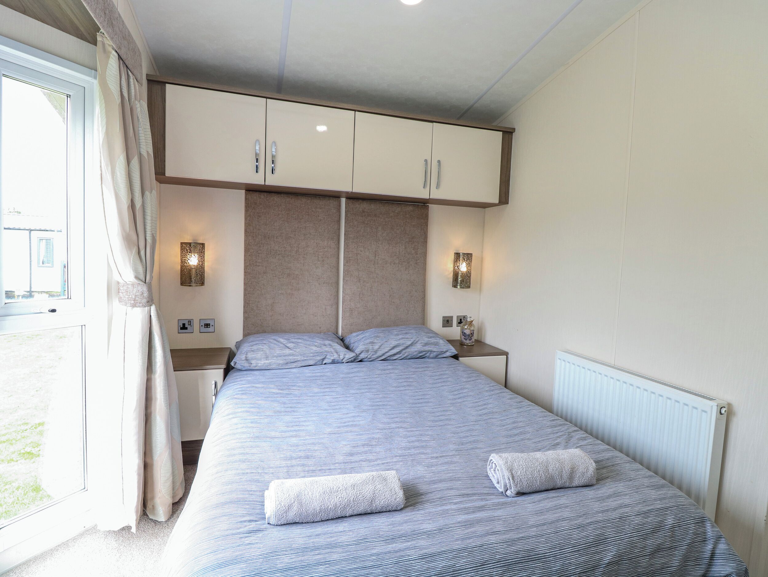 A bedroom with a bed, two bedside tables, a wardrobe, and a window with curtains.