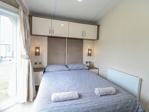 A bedroom with a bed, two bedside tables, a wardrobe, and a window with curtains. - 59 Cliff Field (Lowestoft)