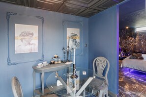 A room with a glass table, a chair, a bed with LED lighting, and artwork on the walls.