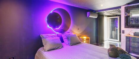 A bedroom with a bed, pillows, a bedside lamp, and a window.