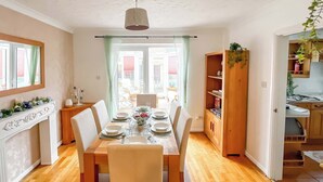 Un comedor con una mesa de madera dispuesta para cuatro, una chimenea blanca y vistas al exterior.