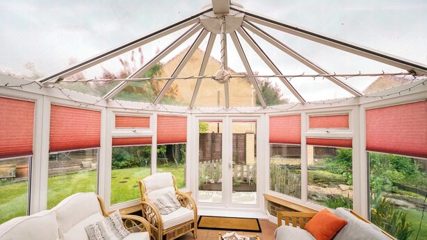 Un invernadero con techo de vidrio, muebles de mimbre y vistas a un jardín.