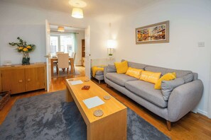 Ein Wohnzimmer mit einer Couch, einem Holztisch, einem Esstisch und einer Küche im Hintergrund.