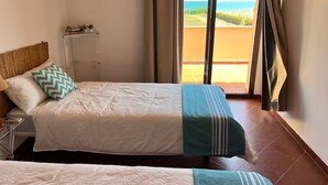 Een hotelkamer met twee bedden, een nachtkastje, een lamp, een raam met uitzicht op de oceaan en een schuifdeur naar het balkon.