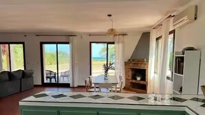 Een ruime woonkamer met een groen keukenblok, een open haard en een eettafel.