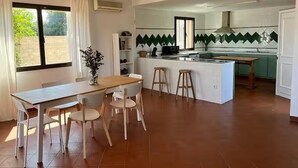 Een moderne keuken met een centraal eiland, een eethoek met een tafel en stoelen, en een groot raam met gordijnen.