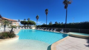 Una piscina con sillas de descanso, palmeras y un edificio al fondo.