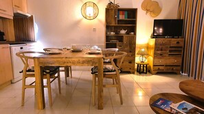 A dining area with a wooden table and chairs, a kitchen in the background, a bookshelf, and a television. - Exceptional, 2-bedroom apartment, waterfront, sea view (Fréjus)