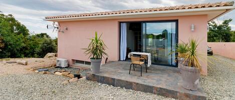 A small building with a tiled roof, a glass door, and a patio area with a table and chairs.
