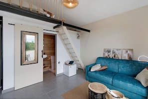 A modern living room with a blue sofa, a staircase, and a large mirror.