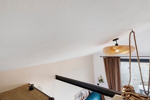 A room with a hanging rattan light fixture, a black metal beam, a brown curtain, and a window with a view.