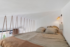 A bedroom with a bed, a hanging light fixture, and a view of the outside.