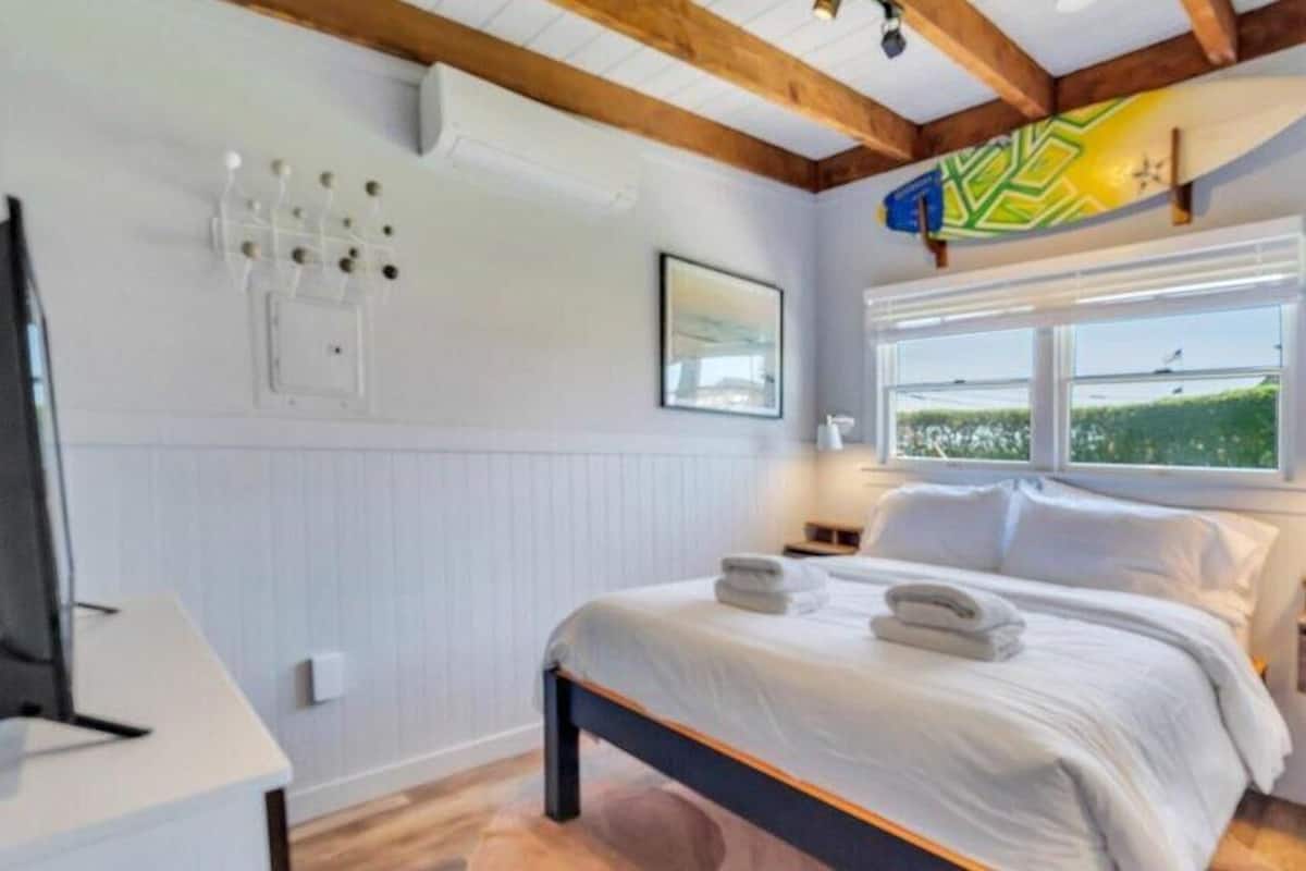 Une chambre à coucher comprenant un lit, des tables de chevet, une fenêtre avec vue et un plafond avec des poutres apparentes.