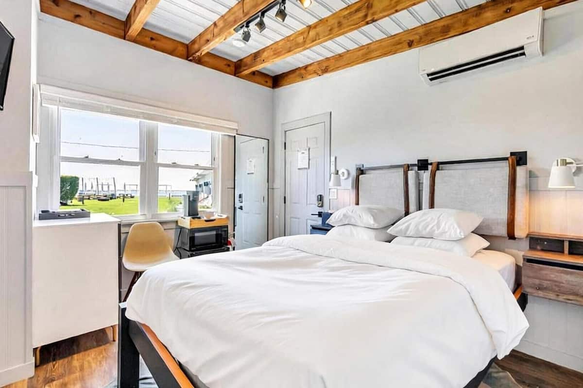 Une chambre à coucher avec un grand lit, un bureau, une chaise et une fenêtre donnant sur un paysage verdoyant.