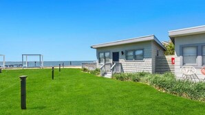En fastighet som ligger vid stranden, med en gräsyta, en liten byggnad med en veranda och fri utsikt över havet.