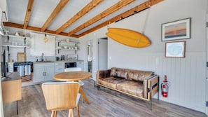 A modern kitchen with white cabinets, a wooden dining table, and a leather sofa.