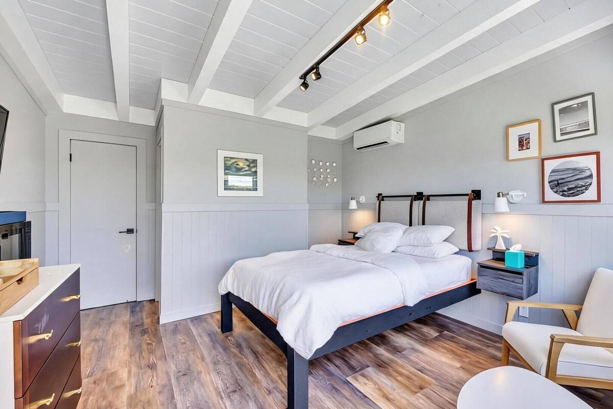 Une chambre à coucher moderne, avec un lit, des tables de chevet, une chaise et des œuvres d’art accrochées aux murs.
